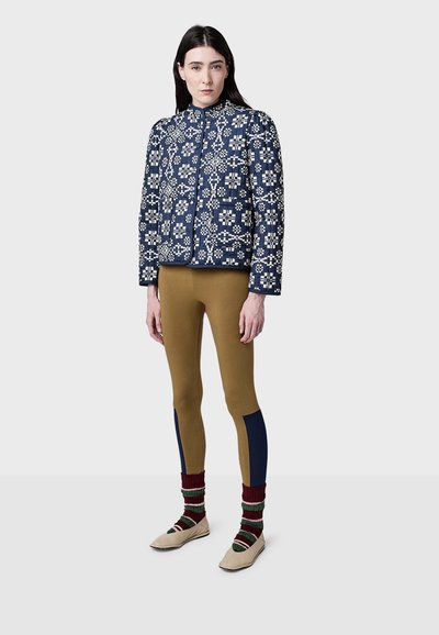 Prešívaná námornícka bunda s bielym kvetinovým vzorom, hnedé legíny s námorníckymi akcentmi a multicolor pruhované ponožky. Bežová obuv dokončuje outfit.