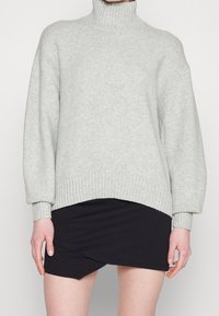 Jasnoszary sweter z golfem z prążkowanym dołem i mankietami, o luźnym kroju i miękkiej fakturze, zestawiony z czarną spódnicą.