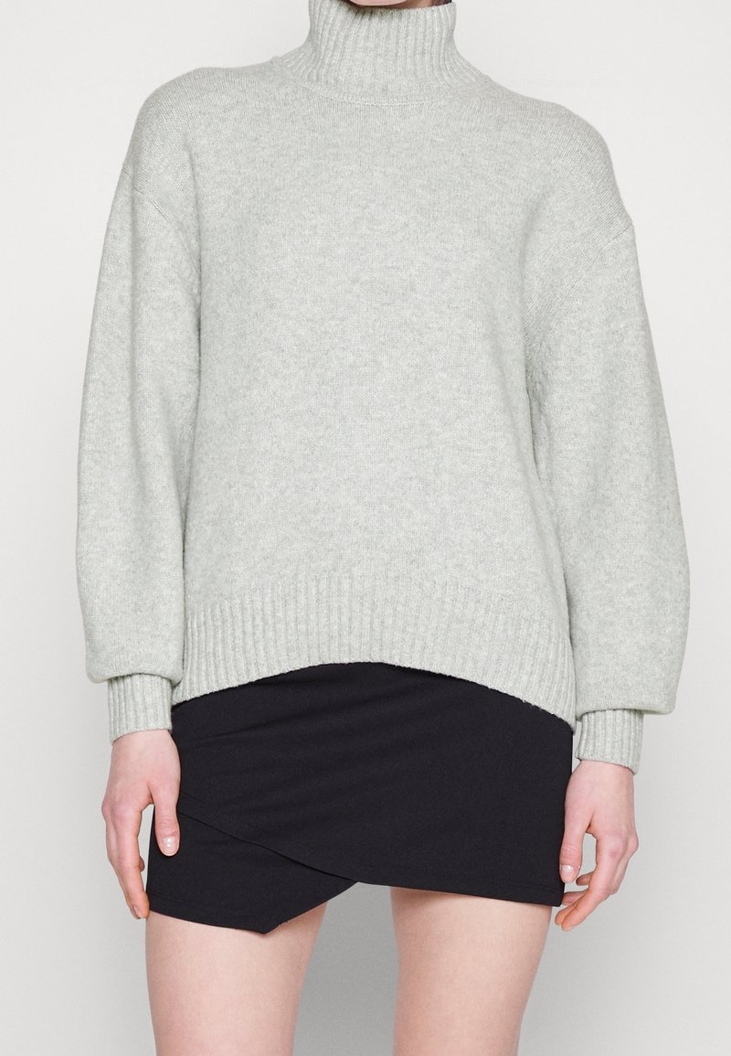 Jasnoszary sweter z golfem z prążkowanym dołem i mankietami, o luźnym kroju i miękkiej fakturze, zestawiony z czarną spódnicą.