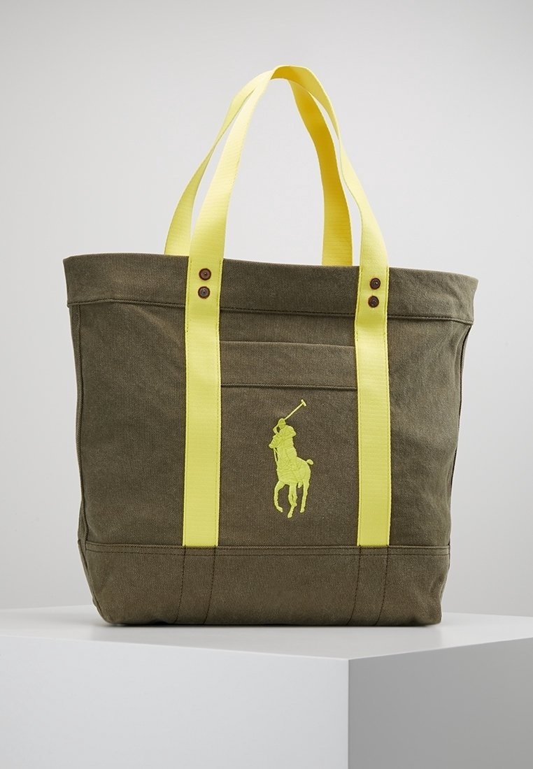 Olivgrön canvas tote-väska med ljusgula handtag. Har en gul broderad logotyp av en polospelare och två bruna knappar på framsidan.
