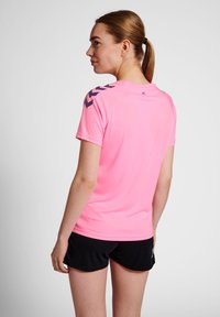 Camiseta deportiva de manga corta en poliéster rosa brillante con acentos en chevron negros en las mangas, combinada con pantalones cortos deportivos negros.
