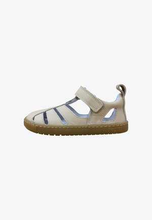 Sandalia de cuero beige con puntera cerrada, laterales recortados, tira de velcro ajustable y suela de goma marrón, diseñada para la comodidad de los niños.