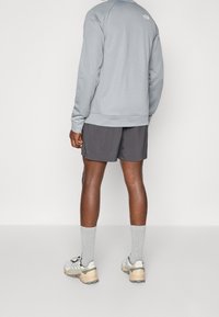 Harmaa pitkähihainen paita, yhdistetty tummiin shortseihin, harmaisiin sukkiin ja vaaleisiin lenkkareihin. Varustettu minimaalisella brändäyksellä ja yksinkertaisella designilla.