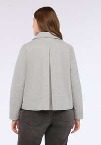 Jachetă gri deschis, structurată, cu pliuri la spate și guler larg. Confecționată dintr-un material texturat, cu mâneci lungi și detalii cusute.