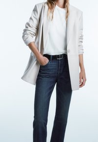 Ljust beige kavaj, vit t-shirt, mörka denimjeans; kavajen har en skräddarsydd design och en enkel knäppning, slim-fit jeans med minimalistisk detalj.