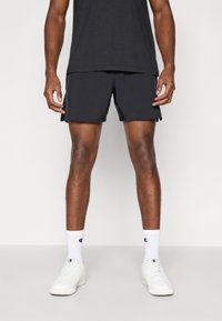 Pantalones cortos deportivos negros con una textura suave, ventilaciones laterales, combinados con calcetines blancos que tienen un logo y zapatillas blancas.