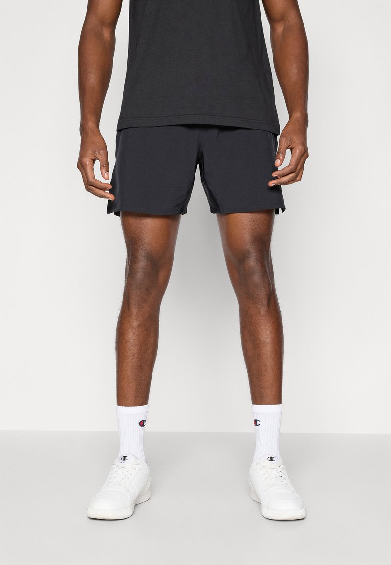 Pantalones cortos deportivos negros con una textura suave, ventilaciones laterales, combinados con calcetines blancos que tienen un logo y zapatillas blancas.