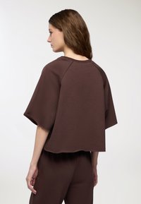 Felpa corta marrone con maniche corte, caratterizzata da una vestibilità rilassata e orlo grezzo. Tessuto morbido con una consistenza liscia.