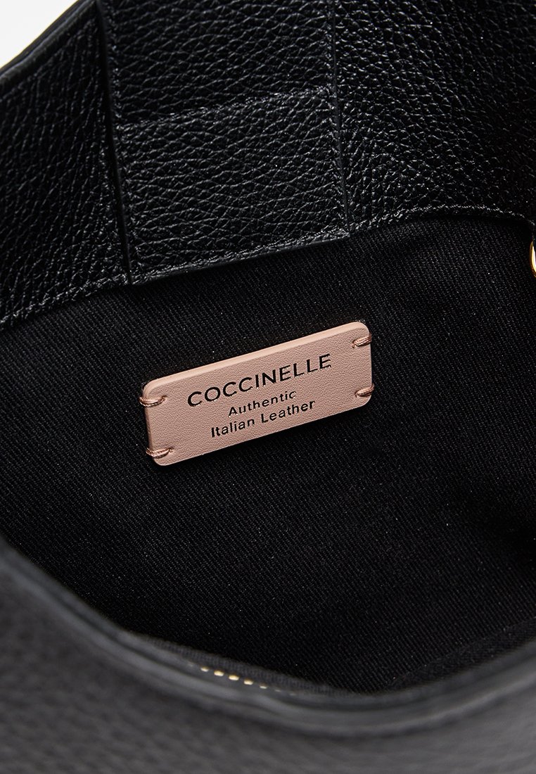 Interno di una borsa a mano in pelle nera con finitura testurizzata e un'etichetta beige che recita "Coccinelle Authentic Italian Leather."