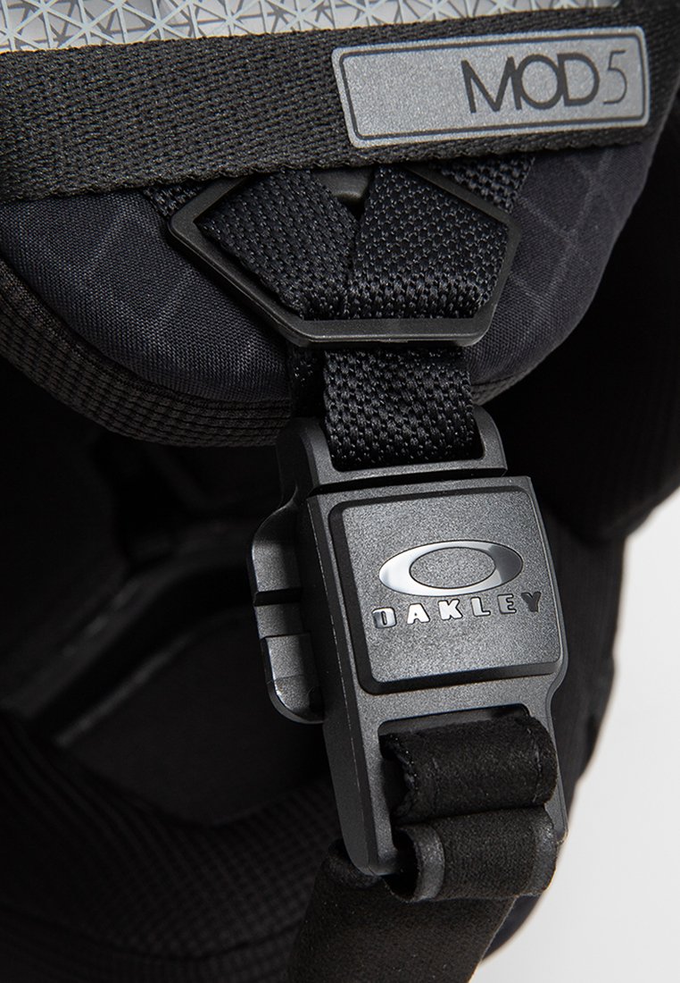 Zwarte verstelbare band met een stevige kunststof gesp met een reliëflogo. Getextureerde stof met een geometrisch patroon op de achtergrond.