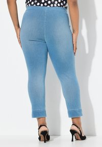 Modré úzké džíny s vysokým pasem, zkrácenou délkou a jemným vyblednutím. Nosené s černými sandály na vysokém podpatku, které podtrhují upravenou siluetu.