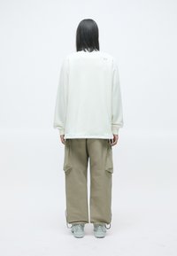 Bílá oversized mikina a khaki cargo kalhoty. Kalhoty mají boční kapsy a detaily se stahovací šňůrkou. Obuv tvoří světle šedé tenisky.