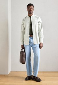 Ανοιχτό πράσινο ριγωτό πουκάμισο πάνω από ένα ελιόχρωμο κορμάκι, ανοιχτό μπλε τζίν, καφέ δερμάτινα παπούτσια και καφέ τσάντα. Απλός σχεδιασμός και άνετη εφαρμογή.