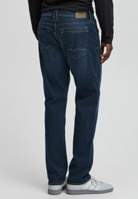 Mørkeblå denimjeans med rett ben, med baklommer med vinklet klaff og en lærmerkelapp på livet.