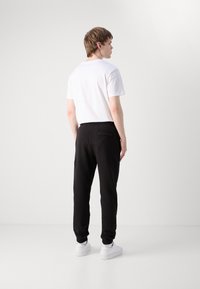 Zwarte sweatpants met elastische boorden, zijzakken en een enkele achterzak, gecombineerd met een eenvoudige witte T-shirt en witte sneakers.