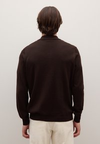 Pullover marrone a maniche lunghe con una texture sottile, caratterizzato da un colletto classico e polsini e orlo a coste, abbinato a pantaloni di colore chiaro.