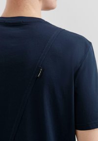 Granatowa koszulka z miękkiej bawełny, z unikalnym wzorem szwów i metką z napisem "TO JEST OS" w pobliżu tylniego dekoltu.