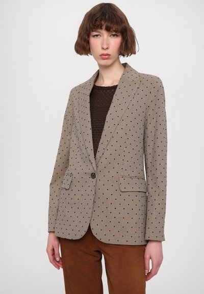Beige blazer med sorte polkaprikker, tekstureret stof, slidskraver, enkelt knaplukning og to frontlommer. Parret med en brun top.