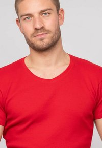 T-shirt rouge côtelé à manches courtes avec un design en V. Le tissu semble lisse avec une silhouette ajustée sur un fond neutre.