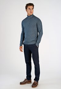 Niebieski, teksturowany sweter z golfem, w połączeniu z ciemnymi spodniami i brązowymi butami. Strój charakteryzuje się dopasowanym krojem i długimi rękawami.