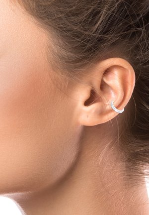 Gros plan sur l'oreille d'une personne à la peau claire et aux cheveux bruns, portant un petit anneau d'oreille en argent sur l'hélix.