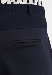 Pantalons marine avec une texture lisse, une taille élastique et une poche arrière discrète avec une ouverture cachée.