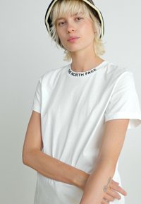 Witte katoenen t-shirt met een ronde hals. Bevat een zwart logo tekst "THE NORTH FACE" op de kraag. Eenvoudig ontwerp, korte mouwen.