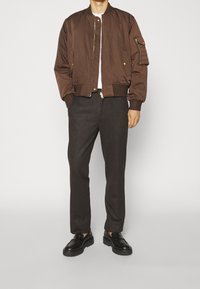 Brown bomber jacket with a front zipper, ribbed cuffs, and two side pockets. Paired with gray tailored pants and black shoes.