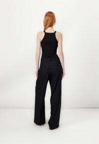 Black sleeveless top paired with high-waisted black wide-leg trousers. The trousers feature a subtle pinstripe pattern and pockets.