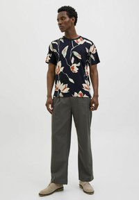 Mėlynas marškinėliai trumpomis rankovėmis su gėlių raštu kreminės ir raudonos spalvų atspalviuose, derinami su pilkais, laisvomis kelnėmis ir smėlio spalvos bateliais.