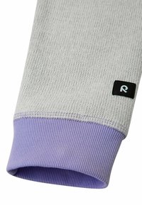Pulsmanschette aus hellgrauem strukturiertem Stoff mit einem lavendelfarbenen Rippbund, versehen mit einem kleinen schwarzen Etikett mit einem weißen "R"-Logo.