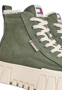 Baskets montantes en suede vert avec une épaisse semelle crème, des lacets crème, une doublure en fausse fourrure blanche et le logo Tommy Jeans sur la languette et sur le côté.