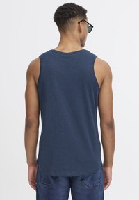 Temno modra majica brez rokavov iz mehkega materiala, z okroglo ovratnikom in širokimi rokavi. V kombinaciji z modrimi jeans kratkimi hlačami, ki nudijo sproščen kroj.