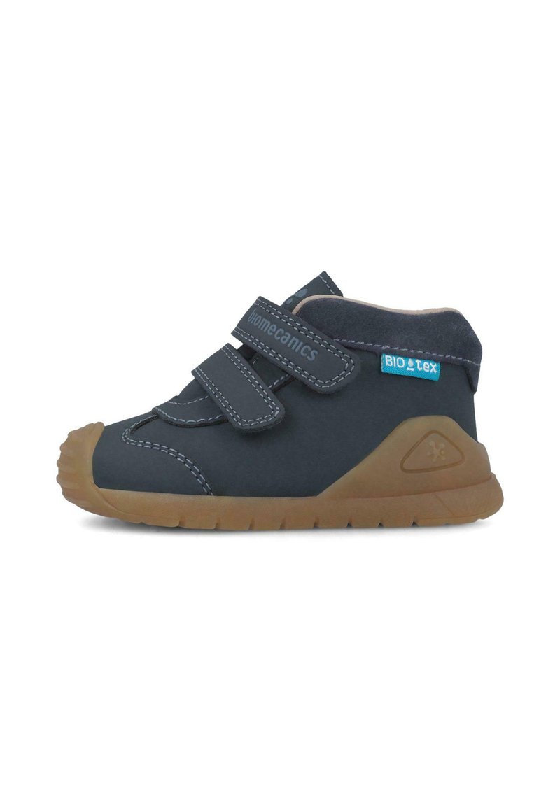 Zapatitos para niño en azul marino con dos correas de Velcro y costuras en gris contrastante. Presentan una suela de goma marrón flexible y un acento texturizado.