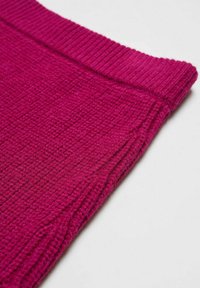 Fuksija teksturirana tkanina z valovitim robom, ki prikazuje pleten vzorec in gladko površino, zložena v enem kotu.