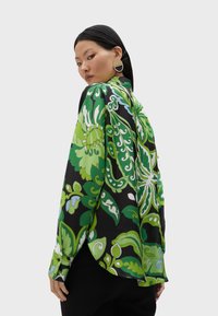 Långärmad skjorta i sidenliknande tyg med stora gröna blommönster på en svart bakgrund. Rundad fåll och knäppta manschetter.
