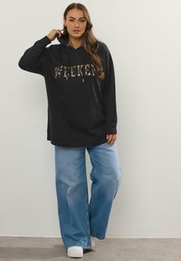 Felpa nera con la scritta "WEEKEND" stampata in un motivo mimetico, dotata di tasca a canguro e cordini. Abbinata a jeans blu a gamba larga.