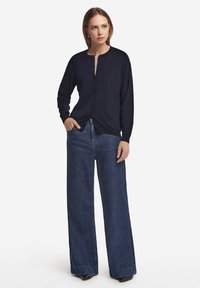 Marinblå knappad cardigan med långa ärmar, kombinerad med högmidjade, vida mörka denimjeans. Slät textur och avslappnad passform.