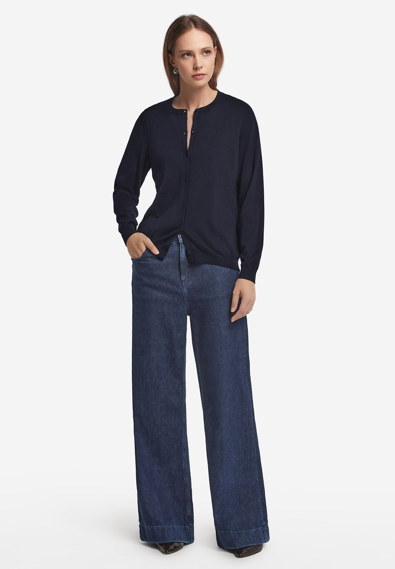 Marinblå knappad cardigan med långa ärmar, kombinerad med högmidjade, vida mörka denimjeans. Slät textur och avslappnad passform.