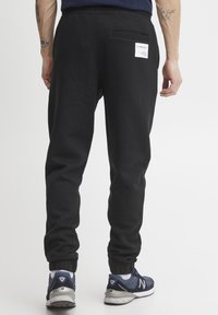 Zwarte sweatpants met elastische tailleband en boorden, voorzien van een achterzak met labeldetail en een effen textuur. Gemaakt in combinatie met sneakers.