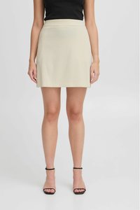 Beige ribbed mini-hame, jonka vyötärö on tiukka, sileä pinta ja siistit reunat, yhdistelemänä mustien nilkkaremmien korkokenkien kanssa.