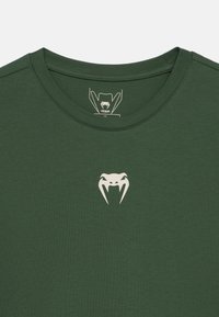 Πράσινο βαμβακερό t-shirt με στρογγυλή λαιμόκοψη και κοντά μανίκια. Διαθέτει λευκό λογότυπο φιδιού στο στήθος. Ομαλή υφή, καθημερινό σχέδιο.