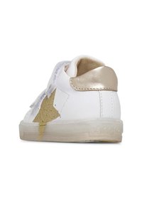 Vit lädersneaker med en framträdande guldstjärndesign, grå kardborreband och metallisk guldklacksdetalj. Genomskinlig gummisul.