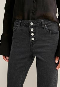 Mustad kõrge vöökohtadega teksad, millel on peenikene siluett, viis nööpi, kaks esikot, ja pehme denimtekstuur.