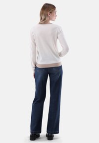 Beiger Pullover mit geripptem Halsausschnitt und Saum, kombiniert mit hochgeschnittenen, dunkelblauen Weitbein-Jeans im klassischen Fünf-Taschen-Design.