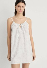 Vestito da notte bianco senza maniche con spalline regolabili, scollatura arricciata e motivo floreale. Tessuto leggero con pizzo lungo l'orlo.