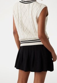 Suéter sin mangas de punto blanco con un cuello y dobladillo de canalé a rayas en blanco y negro, combinado con una falda corta plisada negra.