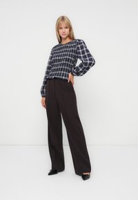 Blouse à manches longues à carreaux bleu foncé et blanc, associée à un pantalon large taille haute brun foncé. Tissu texturé avec des manches bouffantes.