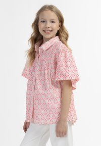 Camicia a maniche corte con bottoni in un tessuto di un rosa chiaro, caratterizzata da un motivo floreale in rosa scuro. Vestibilità rilassata con colletto classico.