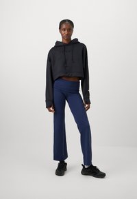 Svart cropped hettegenser med hette og snor, kombinert med marineblå høytliv leggings. Modellen har på seg svarte treningssko.